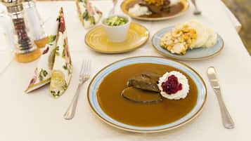 Una mesa dispuesta con platos de comida, incluyendo un guiso con una cucharada de crema y una porción de carne, además de un bol de verduras verdes.