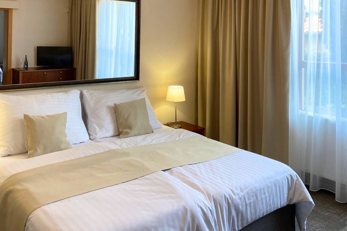 Une chambre d’hôtel avec un grand lit, une lampe de chevet, un téléviseur à écran plat et une fenêtre avec des rideaux.