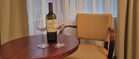 Una mesa de madera redonda con una botella de vino y dos copas, una silla de mimbre y vistas a árboles a través de cortinas traslúcidas.