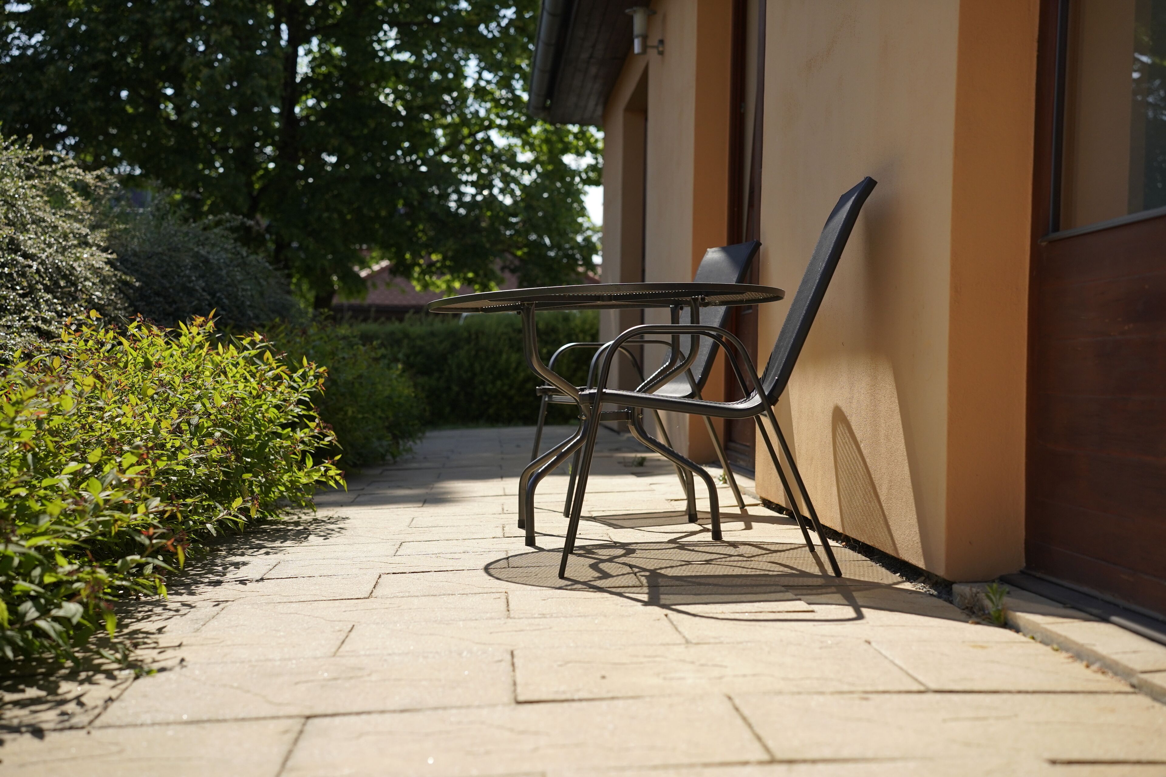 A patio with a table and chairs, a tiled walkway, and a building with a beige wall.