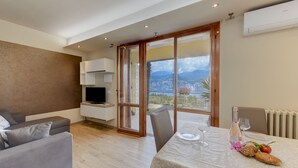 A modern living room with a grey sofa, a flat-screen TV, and a dining area with a table set for two.