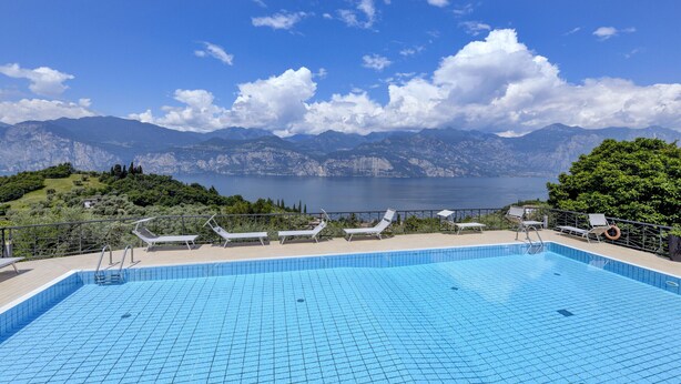 A swimming pool with lounge chairs and a view of mountains and a lake.