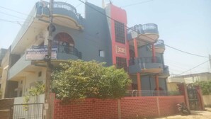 Un immeuble à plusieurs étages doté de balcons, d’un mur en briques et d’une enseigne indiquant « Priyanka Residency Kartik Inn Guesthouse ».