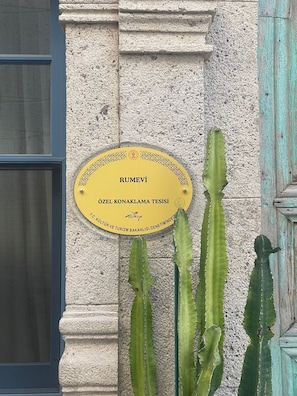 A plaque on a building wall with cacti nearby. - Rumevi (Cesme)