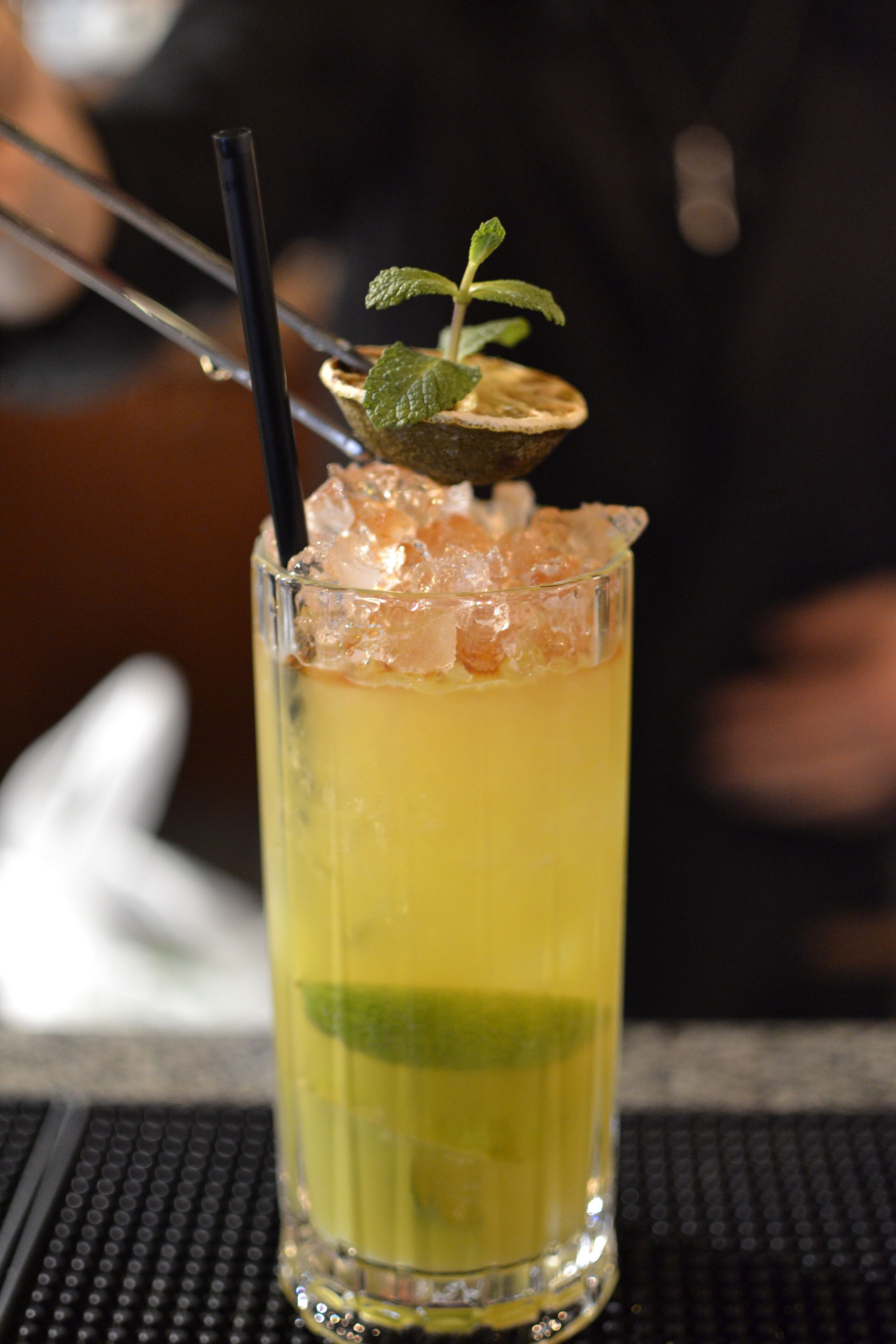 A tall glass with a layered drink, ice cubes, and a mint garnish.