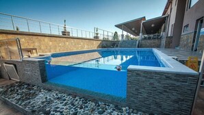 Una piscina con paredes de piedra y borde de piedras, una zona cubierta con escaleras y un letrero de precaución.