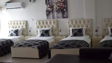 A hotel room with four beds arranged in a row, each with a tufted headboard and patterned bedding. There is a large abstract painting on the wall above the beds.