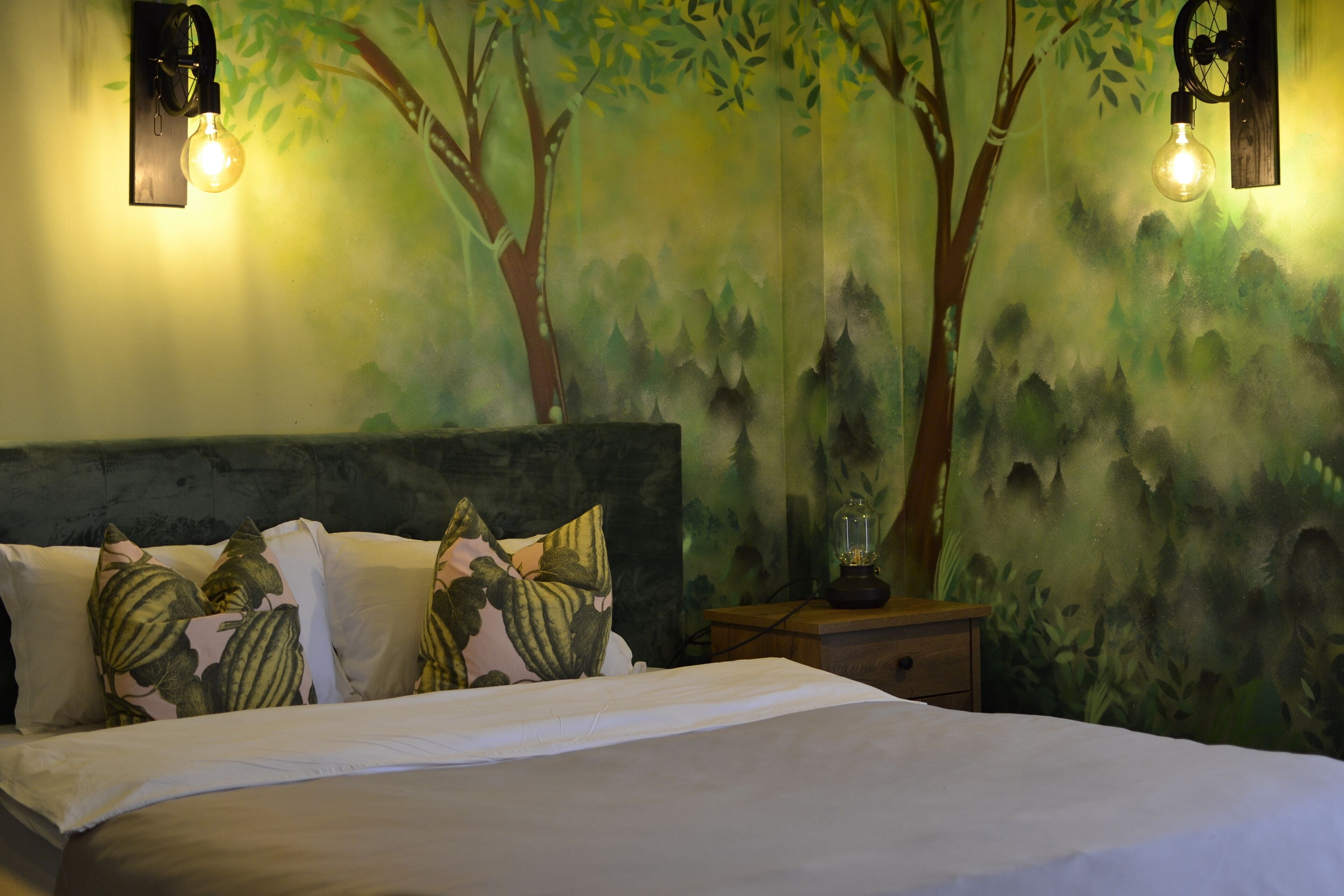 A bedroom with a bed, pillows, a nightstand, and a wall mural.