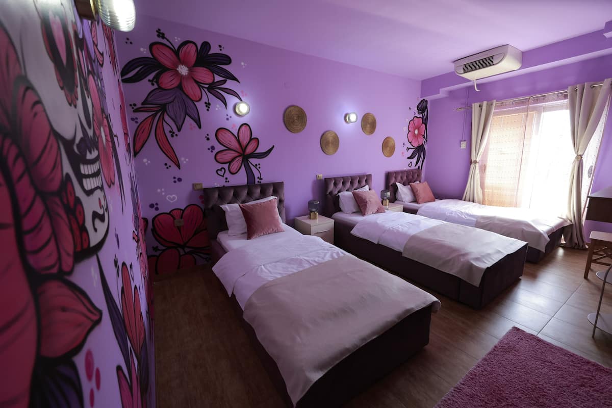 Ein Zimmer mit zwei Betten, einem Wandgemälde und einem Fenster mit Vorhängen.