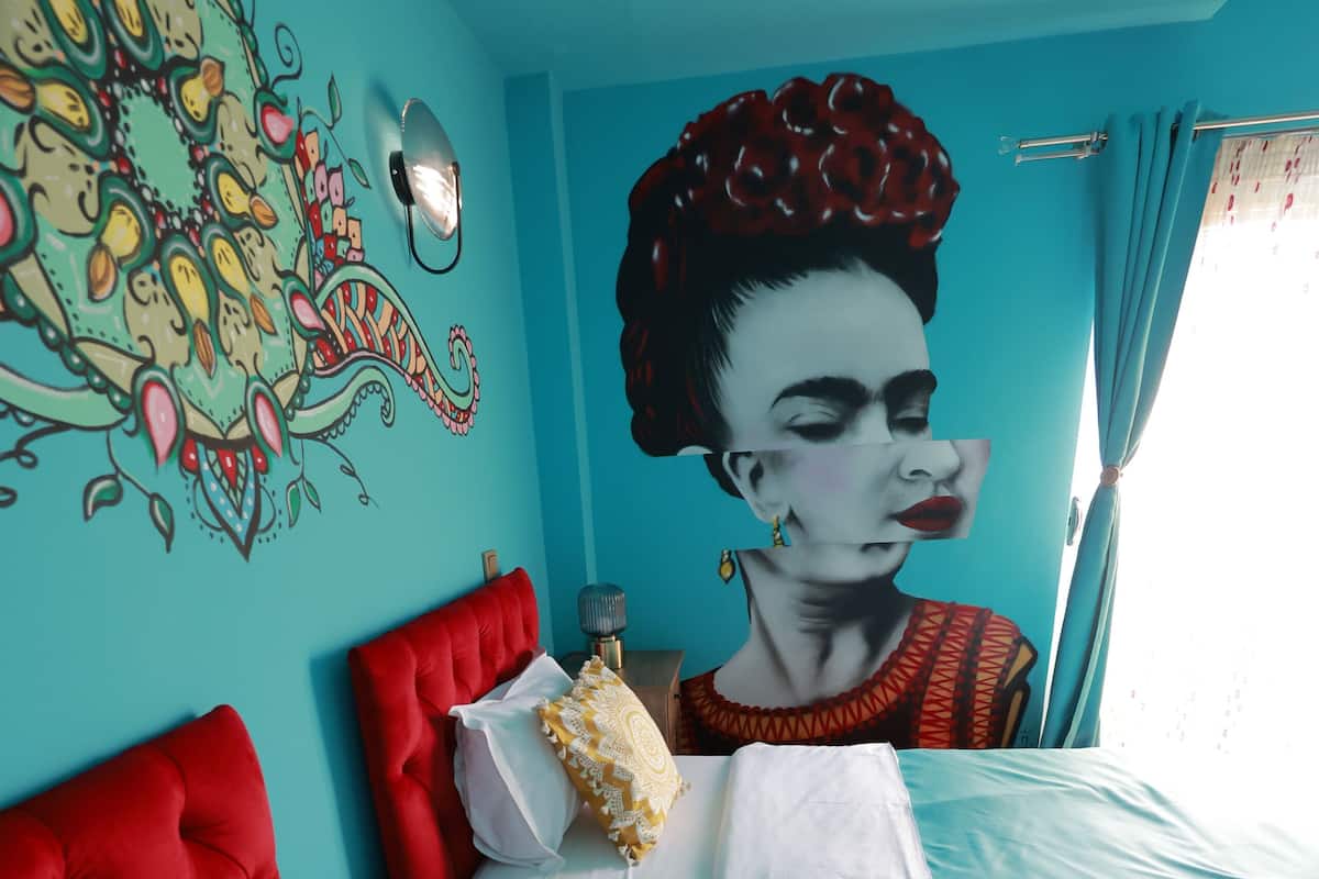 Ein Zimmer mit zwei Betten, Wandgemälde an der Wand und einem Fenster mit Vorhängen.