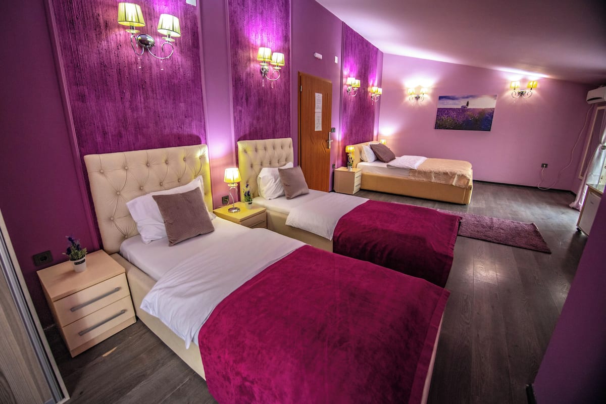 Ein Hotelzimmer mit einem großen Bett, zwei kleineren Betten, einem Nachttisch und einem Spiegel.