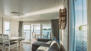 Eine moderne Hütte mit einem großen Schiebeglastür, die auf eine Terrasse führt, einem gemütlichen Sitzbereich mit einer Couch und Sesseln sowie einem Esstisch mit Stühlen.