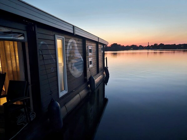 A waterfront building with a large window and a door, a small balcony, and a calm lake in the background.