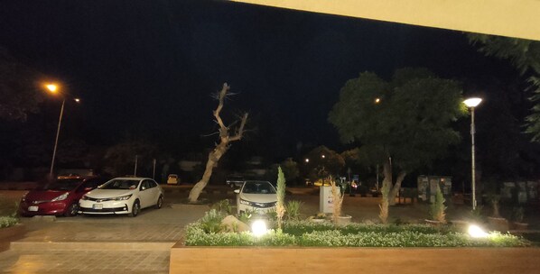 A nighttime parking area with cars, street lamps, and landscaped areas with plants and rocks. - Hotel Star (Islamabad)