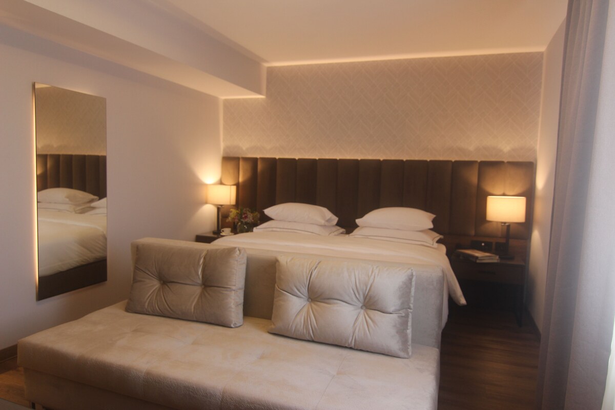 A hotel room with a large bed, two bedside tables with lamps, a sofa, and a mirror on the wall.