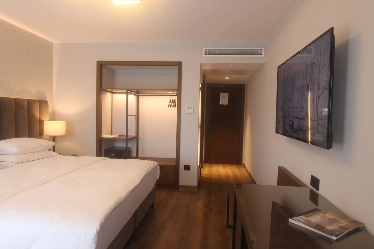 A hotel room with a bed, bedside table, lamp, and a painting on the wall.