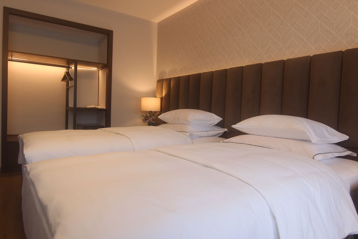 A hotel room with two beds, a large mirror, a nightstand with a lamp, and a patterned wall.