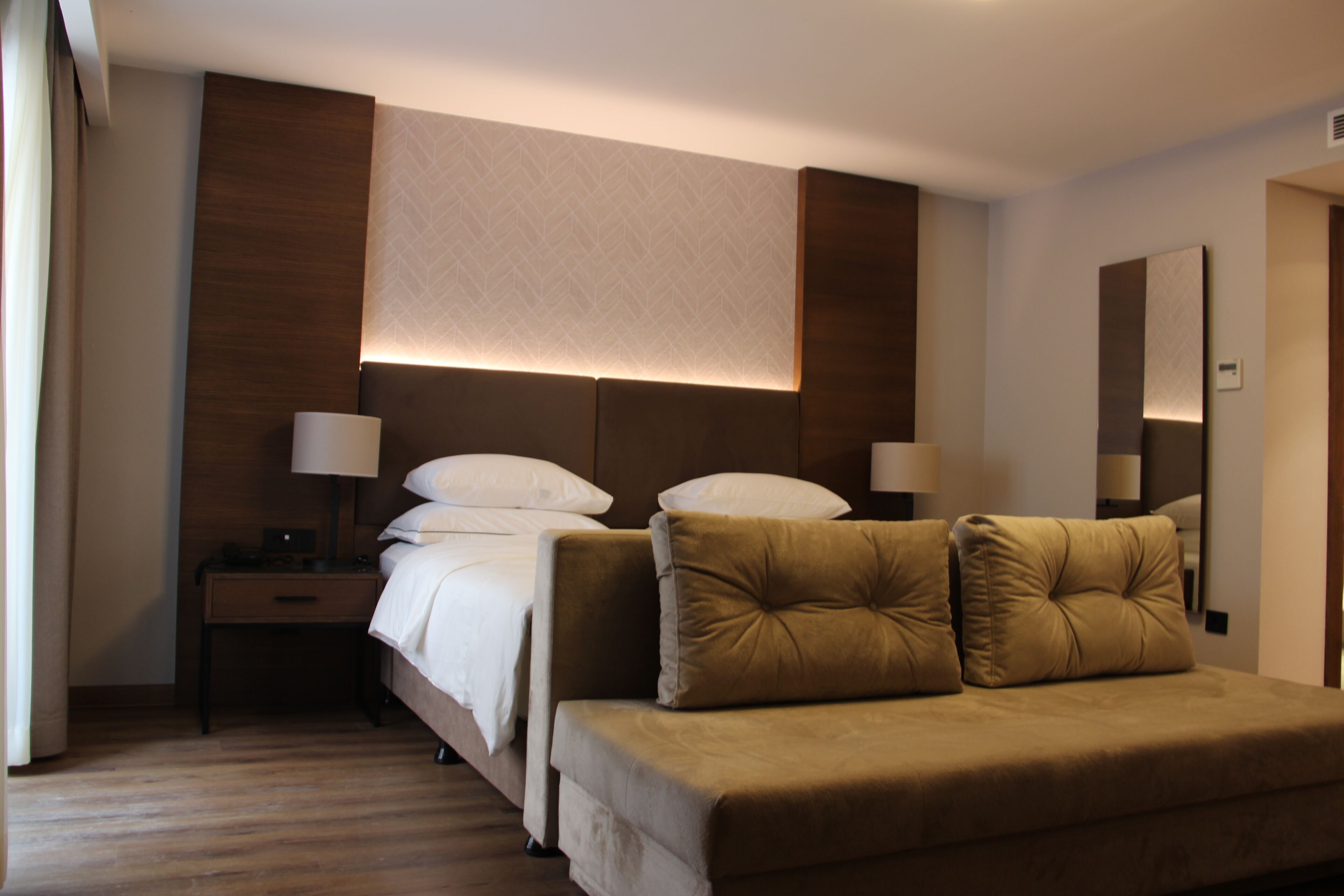 A hotel room with a bed, bedside tables, lamps, a sofa, and a large mirror.