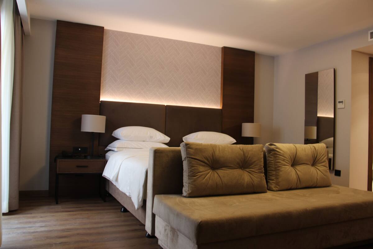 A hotel room with a bed, bedside tables, lamps, a sofa, and a large mirror.