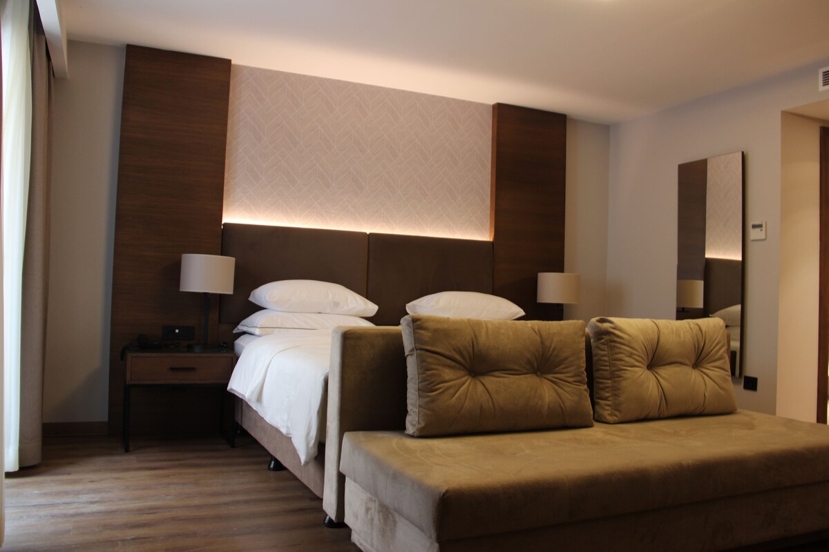 A hotel room with a bed, bedside tables, lamps, a sofa, and a large mirror.
