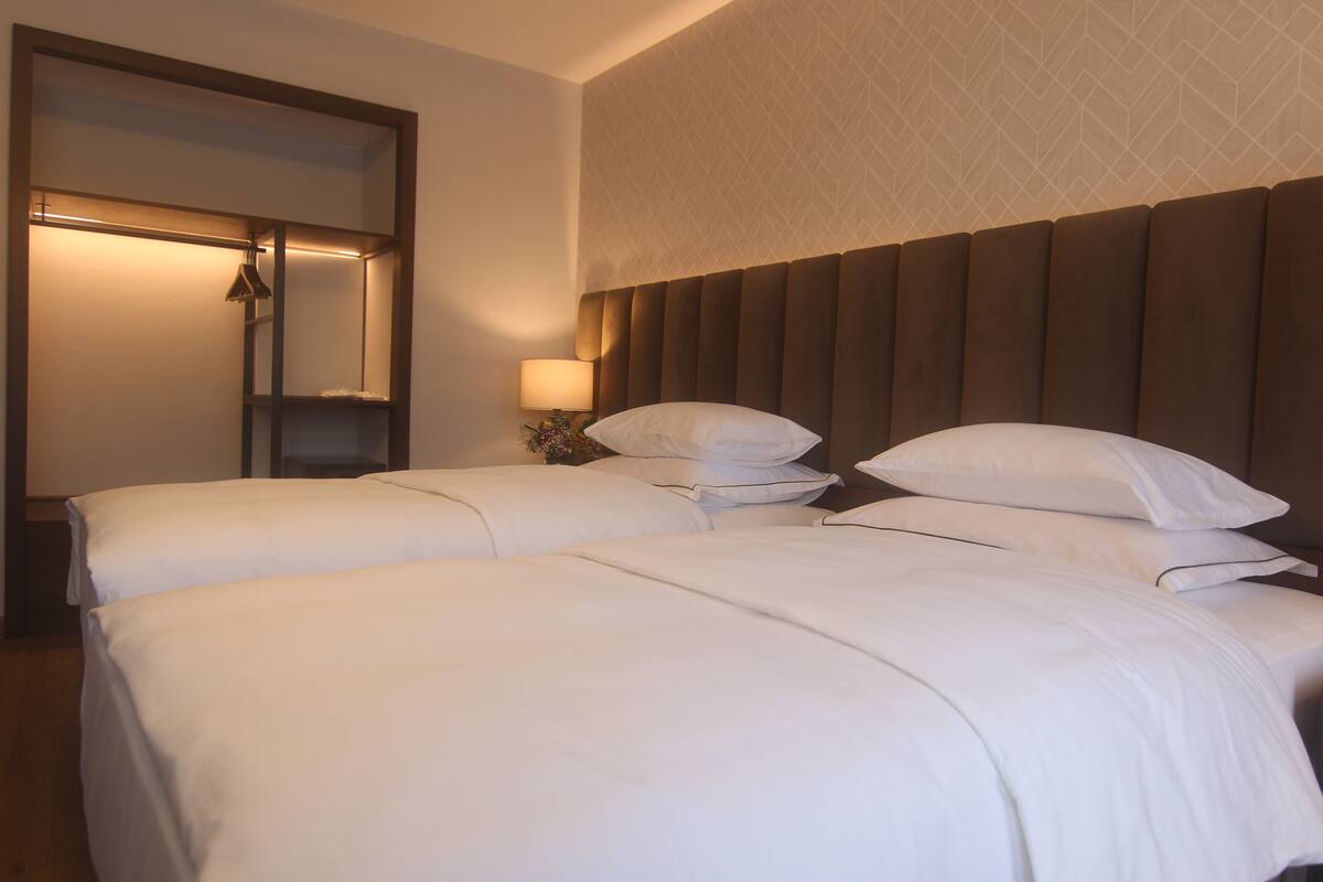 A hotel room with two beds, a large mirror, a nightstand with a lamp, and a patterned wall.