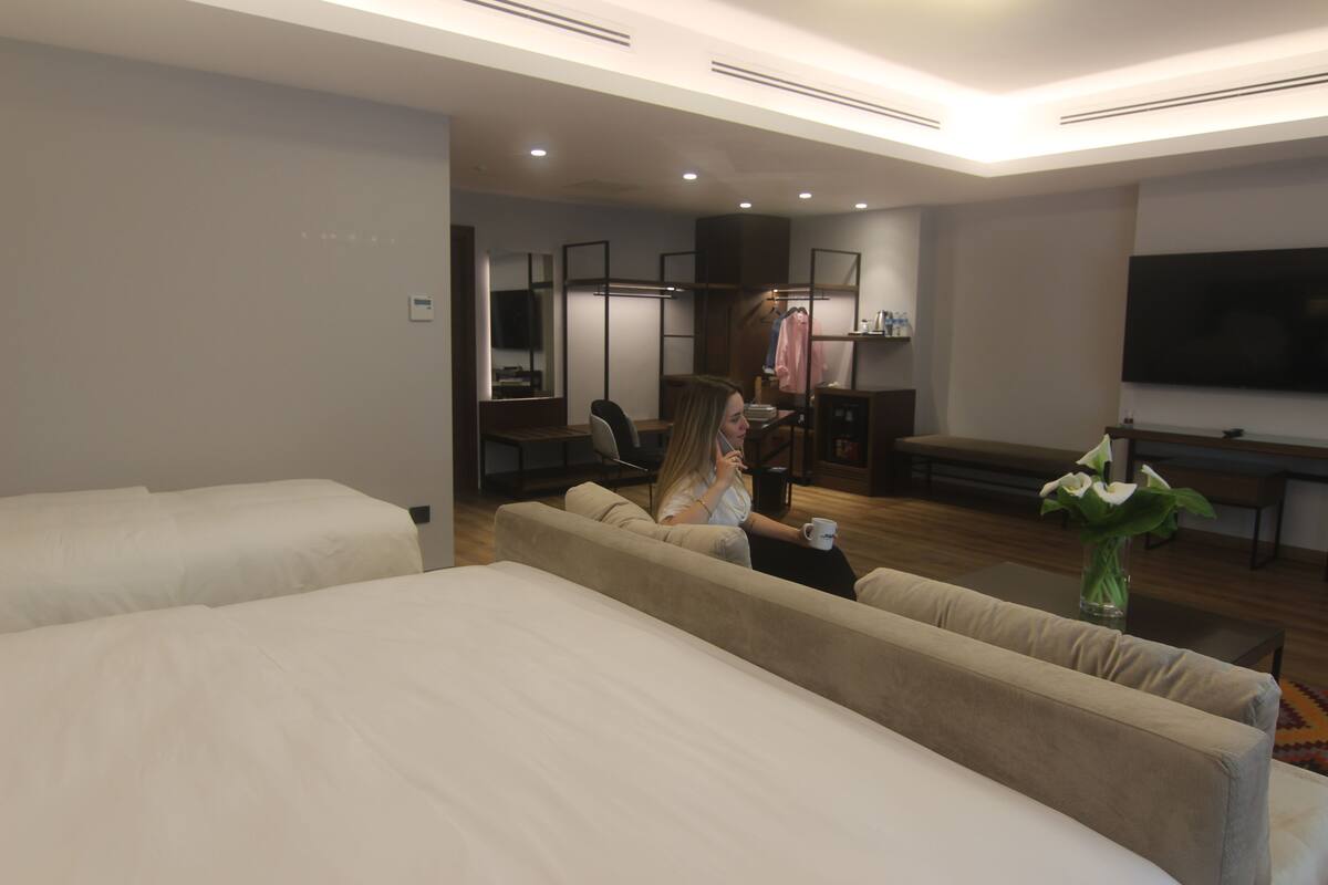 A hotel room with a sofa, a television, a mirror, and a bed.