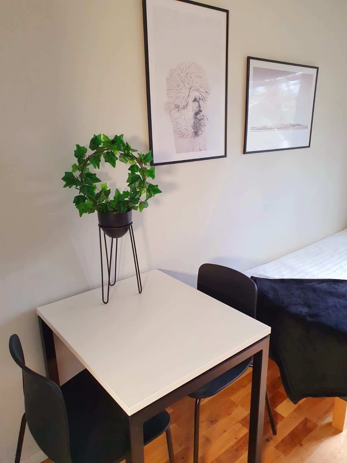 A small, neatly arranged room with a white table, two chairs, a potted plant, and two framed pictures on the wall.