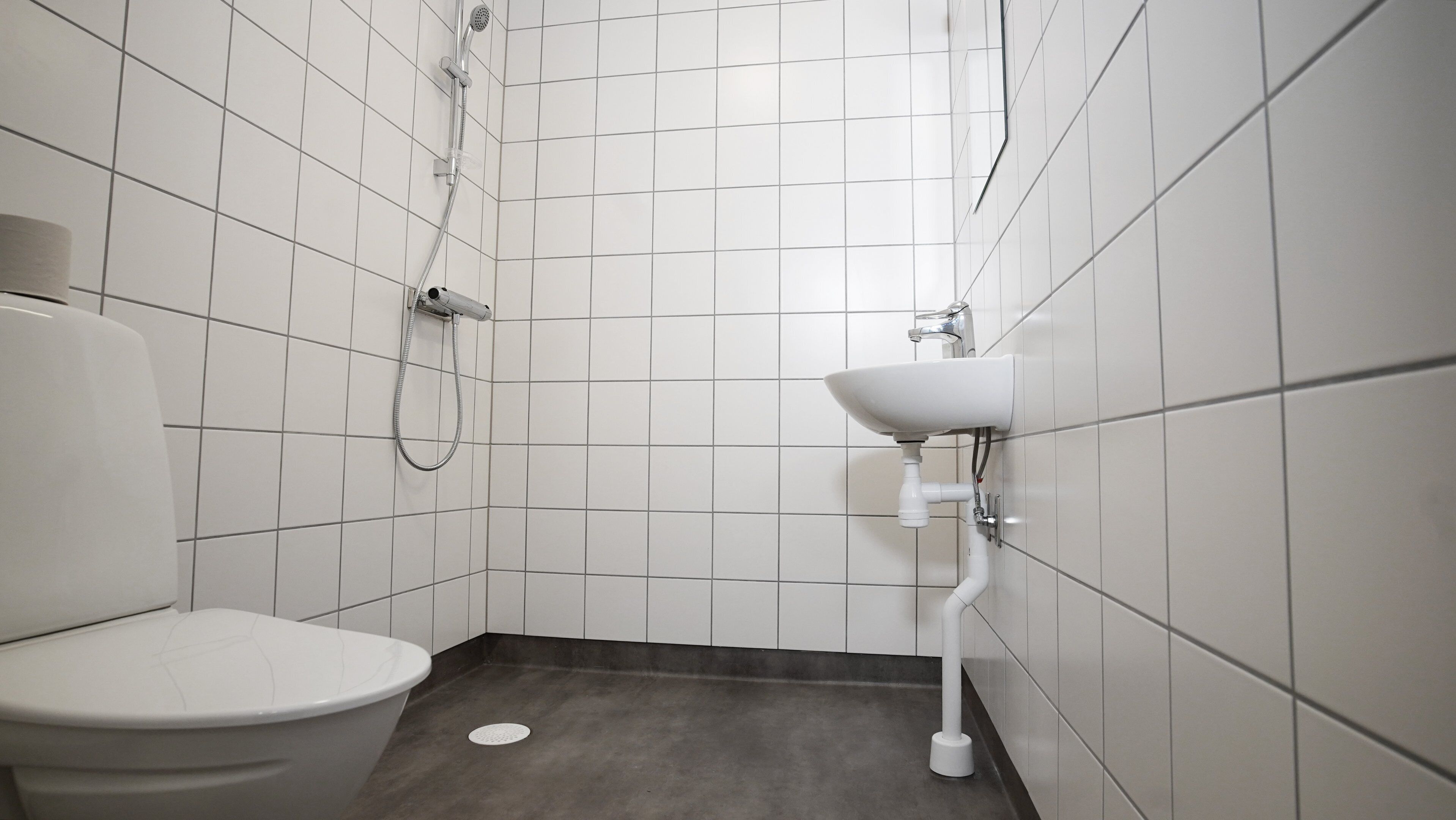 Un baño pequeño y moderno con azulejos blancos, inodoro, lavamanos y ducha.