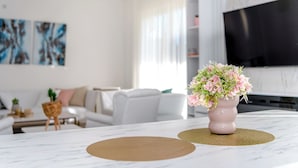 A modern living room with a white sofa, a coffee table, and a TV mounted on the wall. - Green Hills Resort (Hadzici)