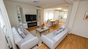 A modern living room with a sofa set, a flat-screen TV, and a dining area with a table and chairs. - Green Hills Resort (Hadzici)