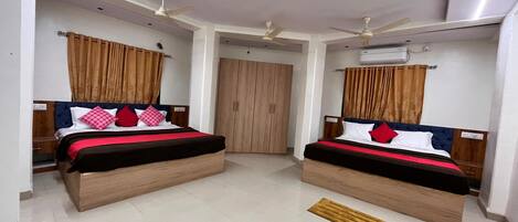 A hotel room with two beds, a wardrobe, a ceiling fan, and an air conditioning unit.