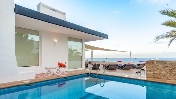 Area piscina moderna con vista aperta sul mare, prendisole e muretto in pietra.