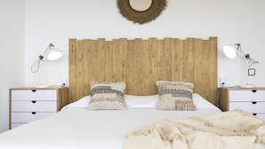 Camera da letto con testiera in legno, due comodini con lampade, un letto con cuscini decorati e un elemento decorativo circolare a parete.