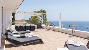 Un balcone con poltrone prendisole, un barbecue e vista sul mare.