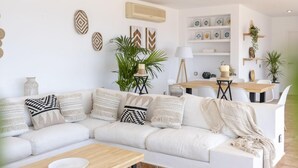 Un soggiorno moderno con un divano bianco, cuscini decorativi, un tavolino da caffè e un'area pranzo con tavolo e sedie in legno.