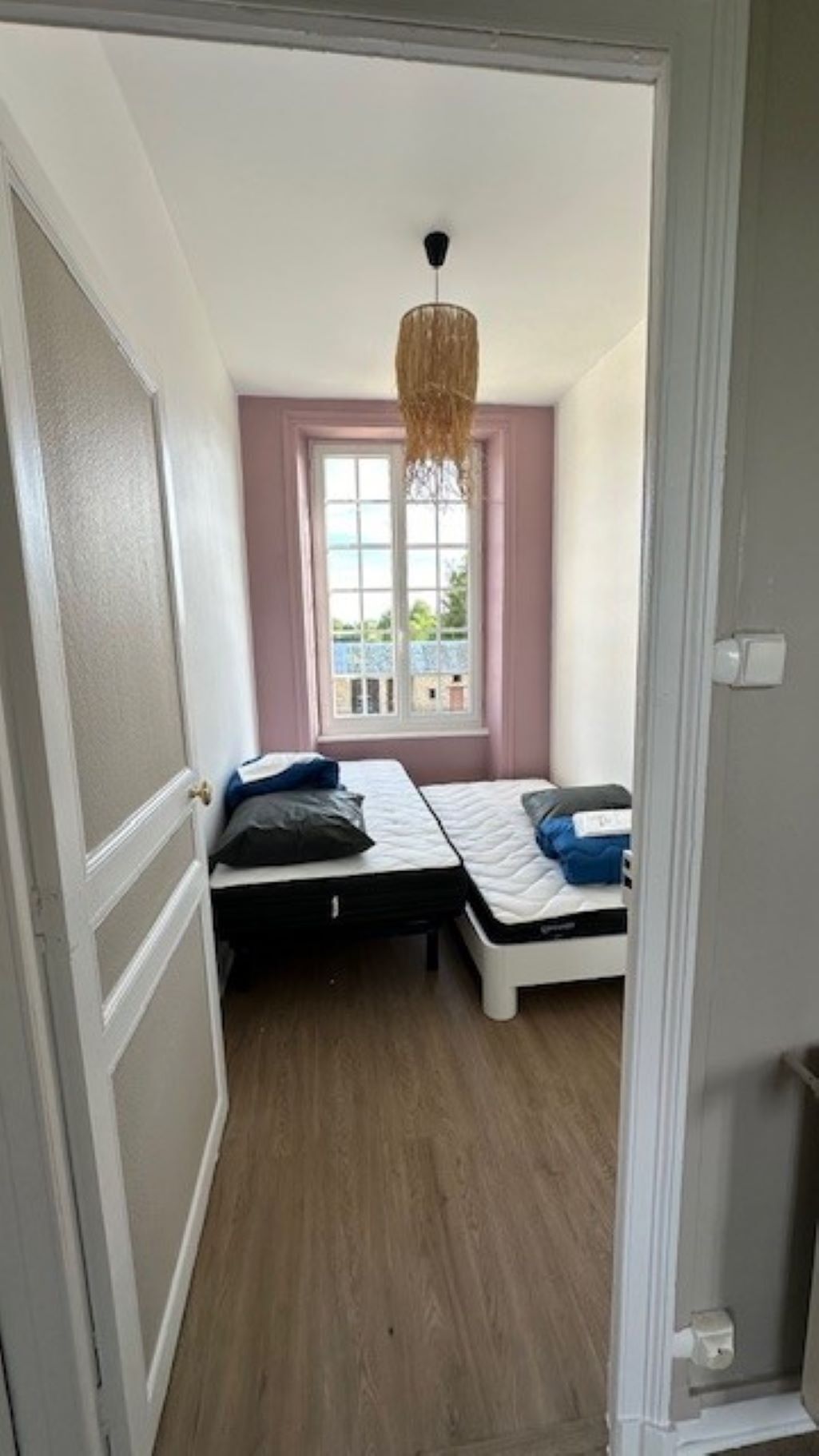 Una habitación pequeña con dos camas individuales, una ventana con vistas y una lámpara colgante.