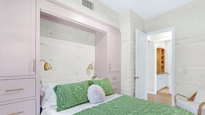 A bedroom with a bed, green and white pillows, a green blanket, a pink wardrobe, and a white nightstand.