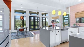 A modern kitchen with large windows, a dining area, and a central island.