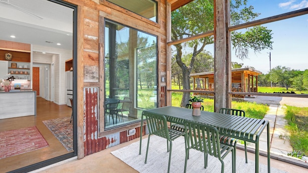 A modern house with large windows, a dining area with green metal chairs, and a view of the outdoors.