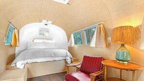 Une petite pièce comprenant un lit, une chaise, une petite table et une lampe.