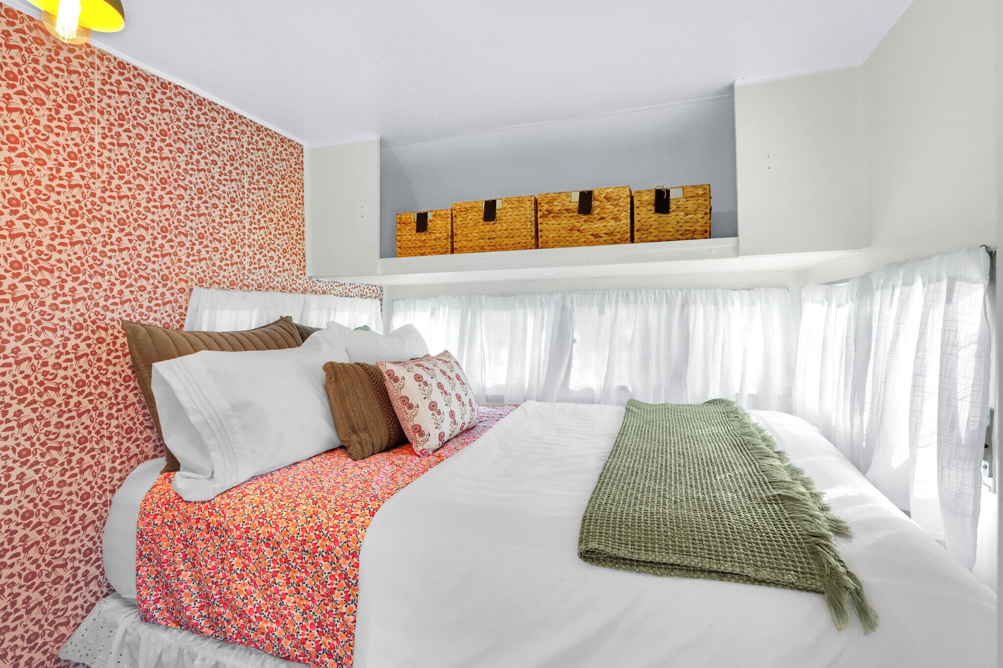 A neatly made bed with a floral bedspread, white pillows, and a green throw blanket.