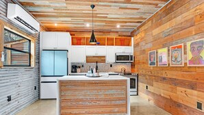 Une cuisine moderne avec un lambris en bois, des armoires blanches, un îlot central et des œuvres d’art accrochées aux murs.