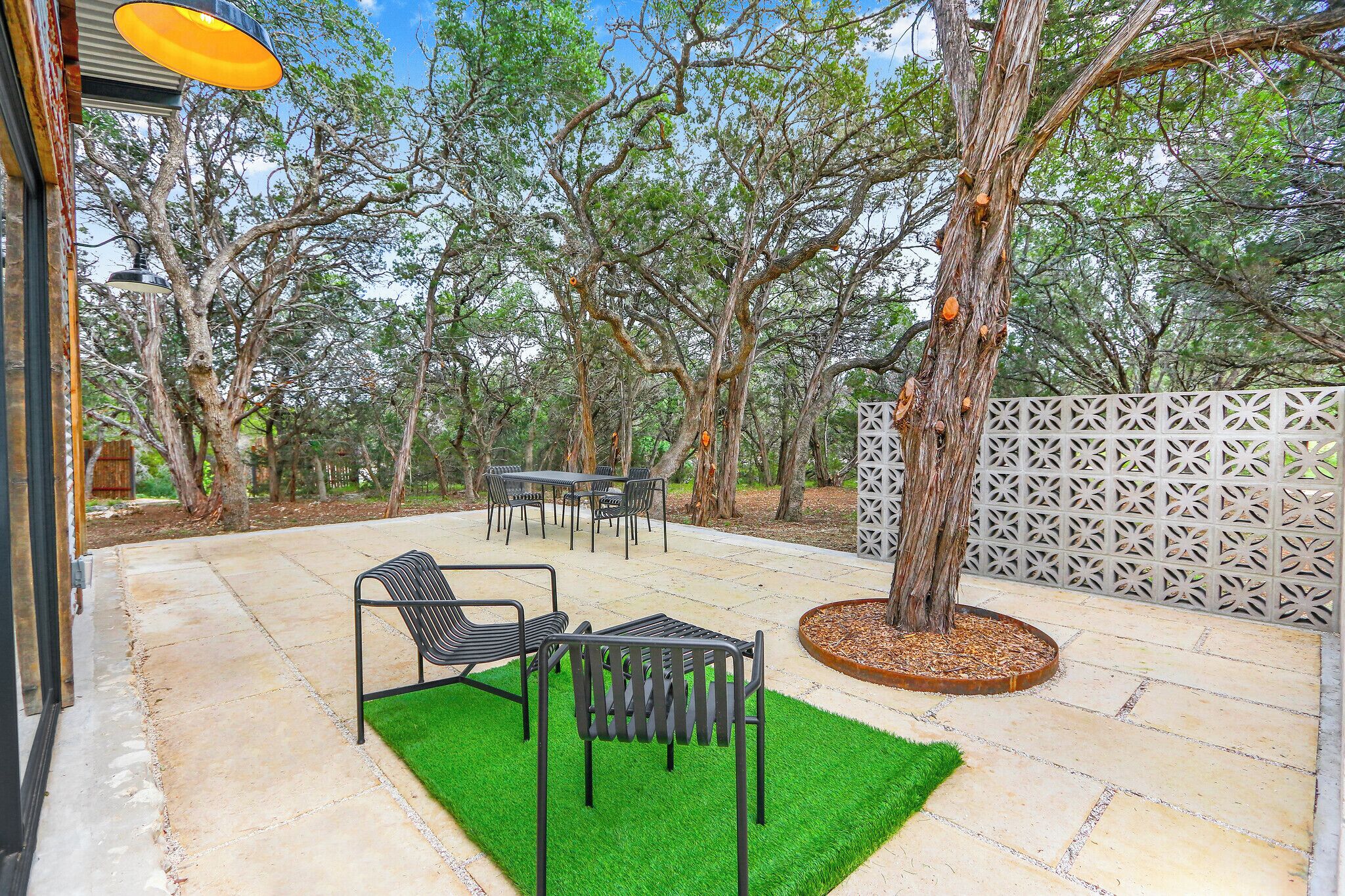 An outdoor patio with a table and chairs, surrounded by trees and a decorative fence.
