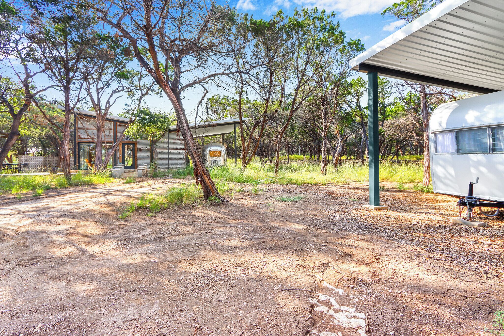 A rustic campsite with a caravan, a small wooden structure, and a covered area.