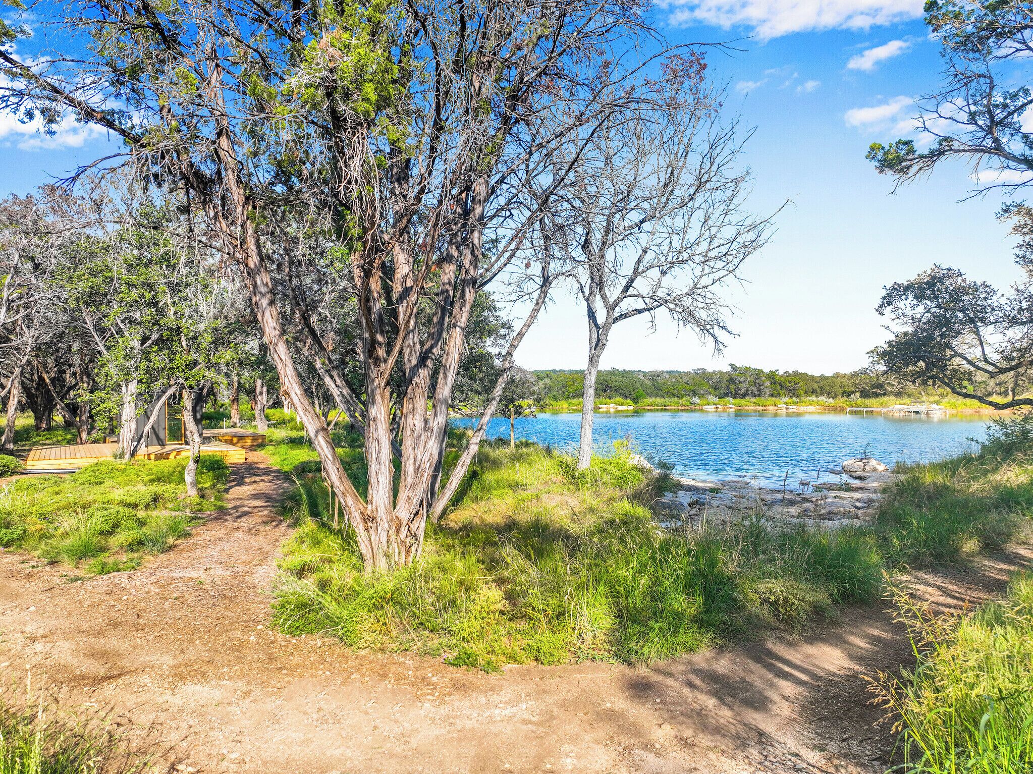 Un paisaje natural con un sendero de tierra que lleva a un lago, rodeado de árboles y vegetación.