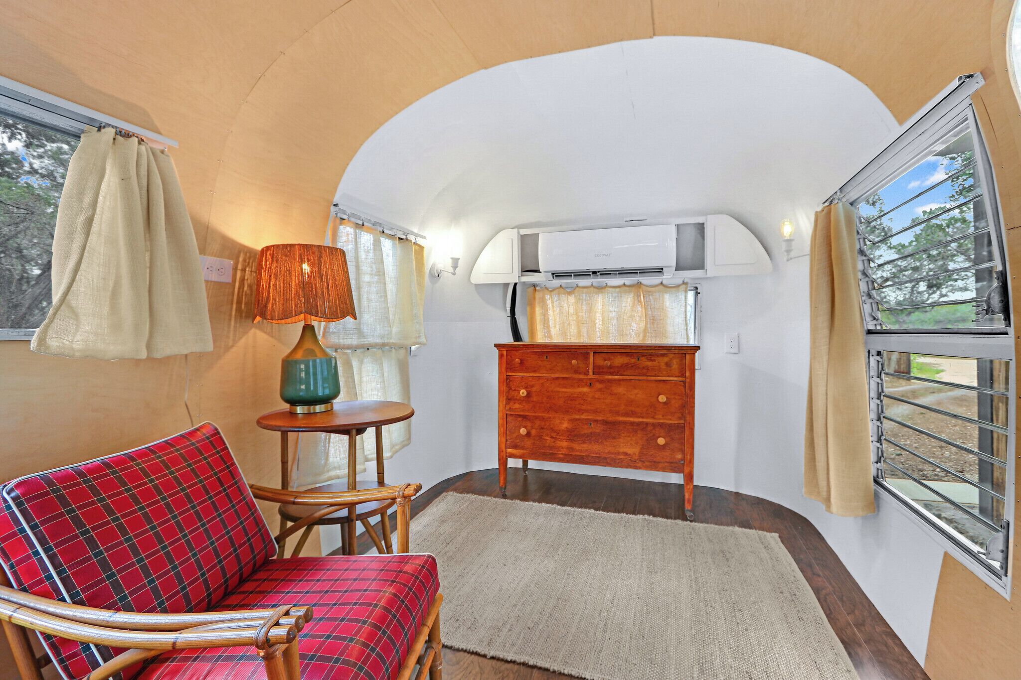 A compact living space with a sofa, a small table, a lamp, a dresser, and a window with curtains.