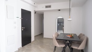 A modern dining area with a rectangular table and four chairs, a black door, and a white wall with a vent. - O&O - 2 BR Stylish & Modern Apartment (Bat Yam)