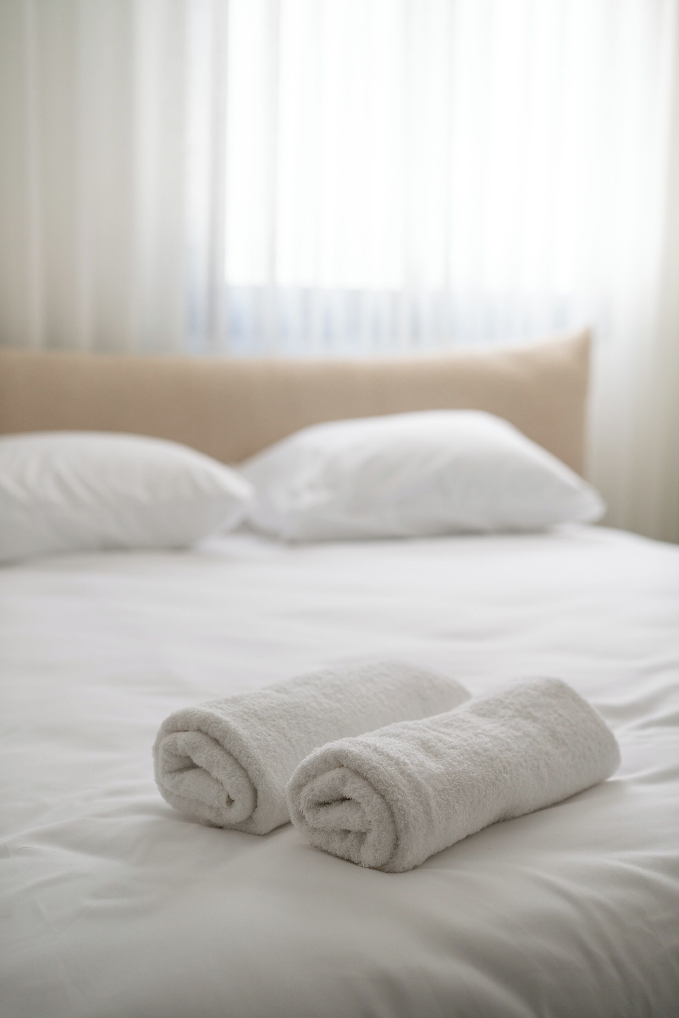 A neatly made bed with two rolled white towels and a beige headboard.
