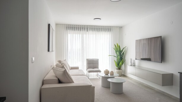 A modern living room with a sofa, armchairs, a coffee table, and a TV mounted on the wall. - O&O - 2 BR Stylish & Modern Apartment (Bat Yam)