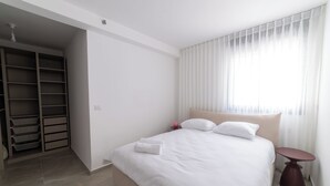 A neatly made bed with white linens, a bedside table, and a wardrobe with open doors. - O&O - 2 BR Stylish & Modern Apartment (Bat Yam)
